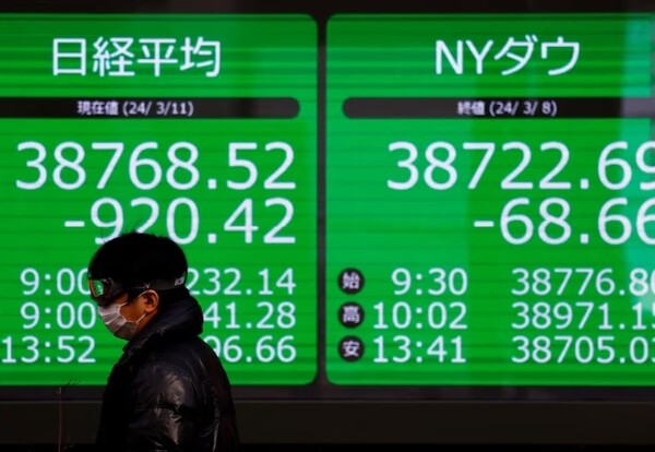 일본 도쿄의 한 증권사 밖에서 행인이 일본 니케이 주가 평균과 다우존스 산업 평균을 표시하는 전광판 앞을 지나가고 있다. 사진=로이터